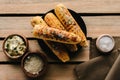 top view of grilled corn on plate near spice salt and butter with parsley on wooden