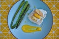 Top view of hake fillet with mango sauce and asparagus. Plate with warm colours and yellow background. Seafood dish