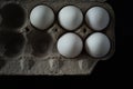 Top view of half carton of fresh white eggs on dark background.