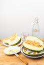 Top view of half green melon, plates with slices and knife on wooden table with bottle and glass of water Royalty Free Stock Photo