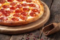 Side view pepperoni pizza on a wooden round board on a wooden background, horizontal