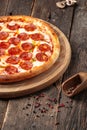 Side view pepperoni pizza on a wooden round board on a wooden background, upright