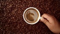 Top view of hand with cup of black coffe put it on coffe beans background