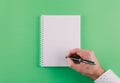 Top view of hand holding ballpoint pen against spiral notepad on green background Royalty Free Stock Photo