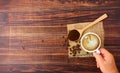 Top view hand holding hot latte coffee in white ceramic cup  with roasted coffee beans  ground coffee on wood spoon on brown sack Royalty Free Stock Photo