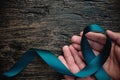 Top view of hand holding teal ribbon on dark background with copy space. Cervical and ovarian cancer, sexual assault, pcos, ptsd