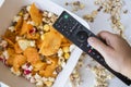 Top view of a hand holding tv remote control against fried popcorn and chips on a bowl Royalty Free Stock Photo