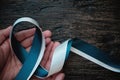 Top view of hand holding white and teal ribbon on dark wooden background with copy space. Cervical cancer awareness month, care. Royalty Free Stock Photo