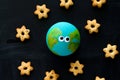 Top view handmade model of Earth planet with funny googly eyes and cookies in the shape of stars on the chalkboard , space and
