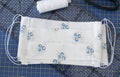 Top view of handmade white fabric cotton face mask on mat with sewing accessories. Protection against saliva, cough, dust,