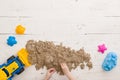 Top view on the hands of a child playing with colorful cookie cutters and kinetic sand on a white table background. The concept of