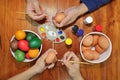 Top view of hands of family members are painting eggs with a paintbrush on wooden table for preparing happy Easter day.