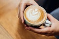 Top view of hands holding a Latte art heart shape served in ceramic cup on wooden table Royalty Free Stock Photo