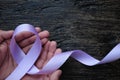 Top view of hands holding lavender or light purple orchid color ribbon on dark wooden background. General and testicular cancer Royalty Free Stock Photo