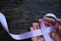 Top view of hands holding lavender or light purple orchid color ribbon on dark wooden background. General and testicular cancer Royalty Free Stock Photo