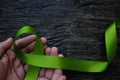 Top view of hands holding lime green color ribbon on dark background. Non-hodgkin lymphoma cancer, lyme disease.