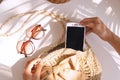 Top view of hands holding smart phone, summer bag and sunglasses on white color background, travel concept. Flat lay, copy space Royalty Free Stock Photo