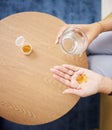 Top view of hands, pills and water in glass for sick woman, iron supplements and cure at home. Capsule tablets
