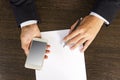 Top view of the hands with smartphone and pen on wooden table with man paper in a business suit. Royalty Free Stock Photo