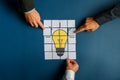 Hands of three businessmen assembling a lightbulb drawn on post it papers