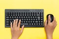 Top view of hands typing on black keyboard and using a mouse on a vibrant yellow background Royalty Free Stock Photo