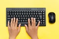 Top view of hands typing on black keyboard and using a mouse on a vibrant yellow background Royalty Free Stock Photo