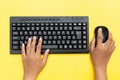 Top view of hands typing on black keyboard and using a mouse on a vibrant yellow background Royalty Free Stock Photo