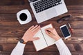 Top view of hands writing in notepad, laptop, phone, pen and glasses on table in office Royalty Free Stock Photo