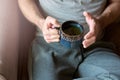 Top view of hands of young caucasian man holding a cup of tea. Enjoying serene morning with hot tea in his living room at home,