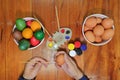 Top view of hands of young happiness man is painting eggs with a paintbrush on wooden table for preparing happy Easter day.