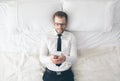 Top view. Handsome businessman with glasses lying on bed texting from his smartphone Royalty Free Stock Photo