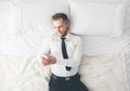 Top view. Handsome businessman lying on bed texting from his smartphone Royalty Free Stock Photo