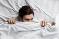 Top view of handsome young man hiding under blanket in bed at home and Royalty Free Stock Photo