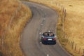 Happy just married couple is driving a convertible car on a country road for their honeymoon, the bride have fun with hands up Royalty Free Stock Photo