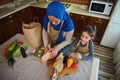 Top view. Muslim woman, loving mom with little daughter unpacking food from supermarket bag together for preparing meal