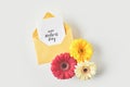 top view of happy mothers day greeting card in envelope and beautiful gerbera flowers on grey