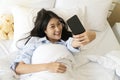 Happy smiling girl using smart phone for selfie on the bed. Beautiful young woman self-portrait with mobile camera lying Royalty Free Stock Photo