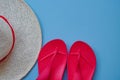 Top view hat with red ribbon and red flip flop sandals on blue background. Summer flatley, composition with copy space, travel and