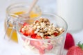 Top view healthy breakfast of homemade granola cereal with milk, strawberry, nuts and fruit, honey with drizzlier on