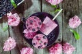 Top view Healthy summer desserts. Ice cream popsicles with black currant, fresh mint and berries, pink wisteria flowers on black p