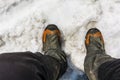 Top view of hiking boots on the feet of a tourist and soiled pants during a mountain trip in the spring snow Royalty Free Stock Photo