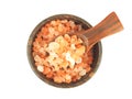 Top view, himalayan pink salt in wooden spoon over brown wood bowl isolated.