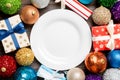 Top view of holiday setting on wooden background. Plate, gifts, baubles and Christmas decorations. New Year dinner concept Royalty Free Stock Photo