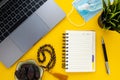 Top view of home office desk. Laptop, empty notebook, pen, dates, rosary beads, face mask, hand sanitizer, green plant on yellow b Royalty Free Stock Photo