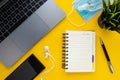 Top view of home office desk. Laptop, empty notebook, pen, mobile phone, earphones, green plant, face mask, hand sanitizer on yell Royalty Free Stock Photo