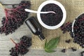 Top view of homemade black elderberry syrup in ceramic jar and bunches of black elderberry with green leaves on wooden desk. Royalty Free Stock Photo