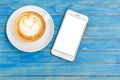 Top view hot latte coffee in white cup and smartphone with blank Royalty Free Stock Photo