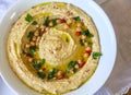 Top view of Humus plate garnished with fresh parsley leaves, red peppers bites, chickpeas, olive oil and sumac