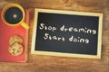 Top view image of blackboard with the phrase stop dreaming start doing, next to coffee cup and cookies