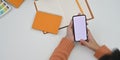 Top view image of creative woman hands holding/using a white blank screen smartphone over white working desk. Royalty Free Stock Photo